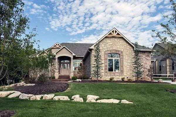 Stone house with arched windows, front porch, and landscaped lawn under a partly cloudy sky