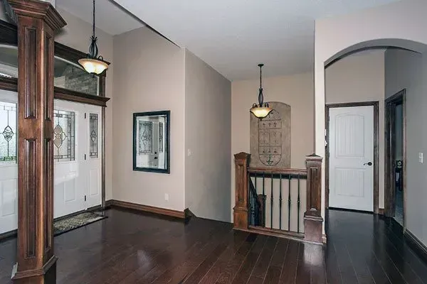 Empty hallway with dark wood floors, white walls, and hanging pendant lights near a staircase opening