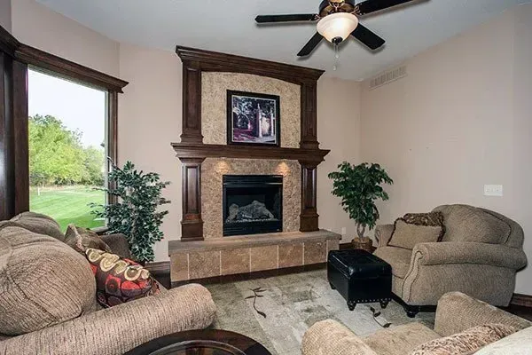 Cozy living room with fireplace, beige sofas, ceiling fan, and large window views