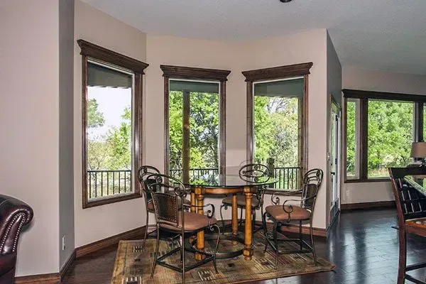 Dining nook with round table and chairs beside large windows overlooking greenery