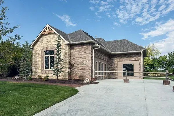 Stone house with arched entry, attached garage, and wide concrete driveway under a blue sky