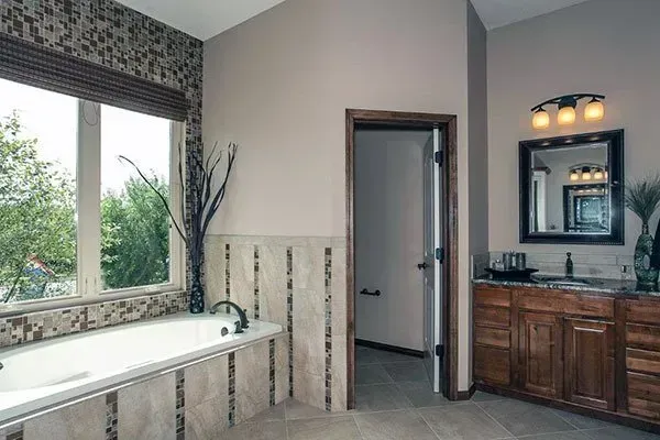 Spacious bathroom with a soaking tub by a window and a wood vanity with mirror lights