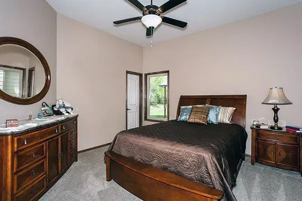 Bedroom with wooden bed, dresser, nightstand, mirror, and ceiling fan in a beige room.