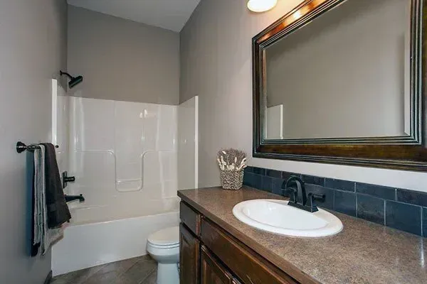 Small bathroom with a white shower, toilet, dark vanity, and large mirror.