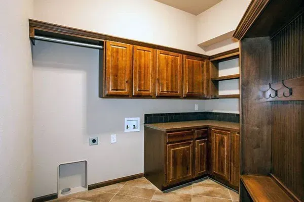 Small office nook with wood cabinets, countertop, and closet-style shelving in a beige room.