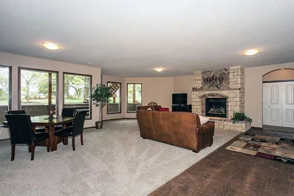 Spacious living room with stone fireplace, brown sofa, dining table, and large windows.