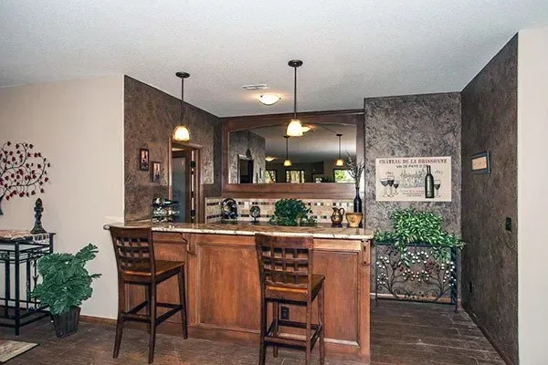 Open-concept kitchen with wood island, bar stools, pendant lights, and gray textured walls