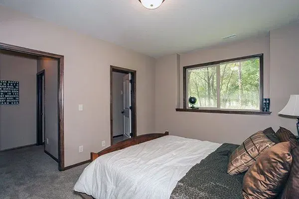 Bedroom with a bed, gray walls, blue carpet, and a window overlooking trees.