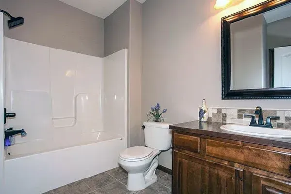 Bathroom with white tub-shower, toilet, and dark wood vanity with mirror.