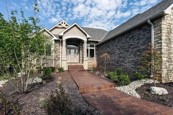 Front entrance of a stone house with a brick walkway and landscaped garden beds
