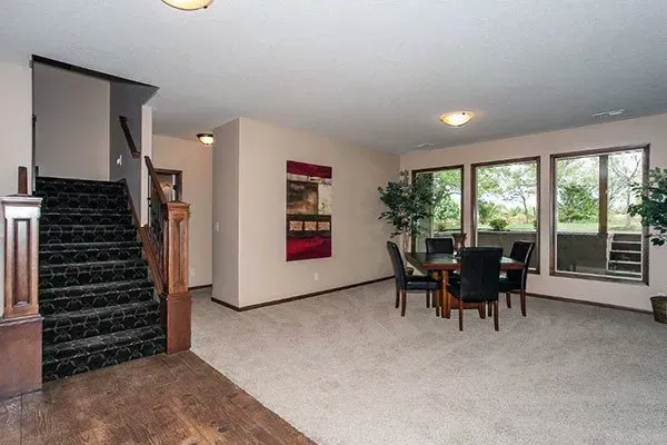 Empty living room with carpeted stairs, dining table, and large windows