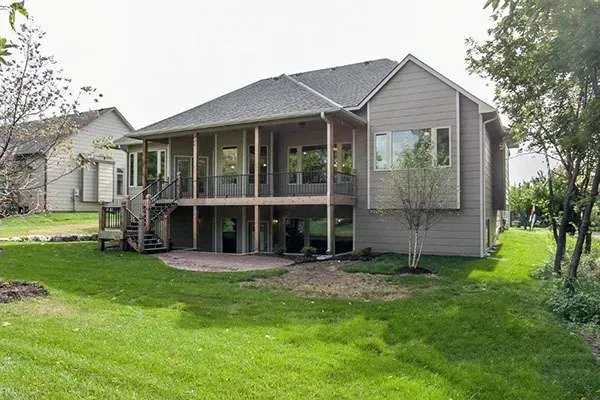 Rear view of a gray house with a raised deck and green lawn in the backyard