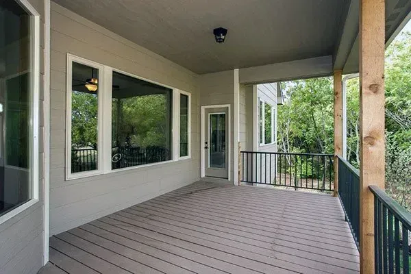 Covered front porch with gray flooring, white walls, large windows, and black railing overlooking greenery