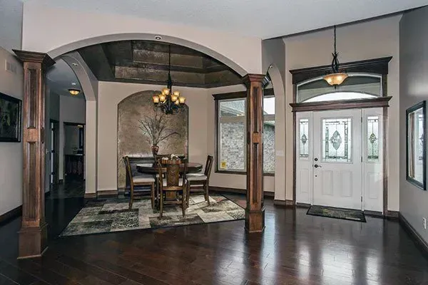 Elegant dining room with dark wood floors, arched columns, and a white front door