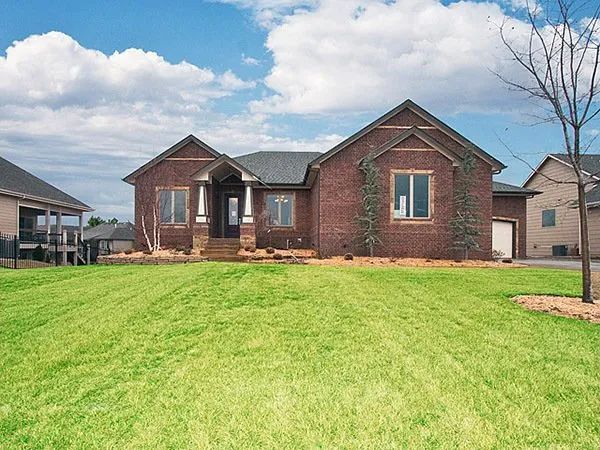 Brick suburban house with a green lawn under a partly cloudy sky