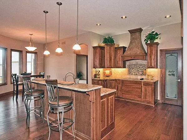 Spacious modern kitchen with wood cabinetry, island seating, pendant lights, and stainless range hood.