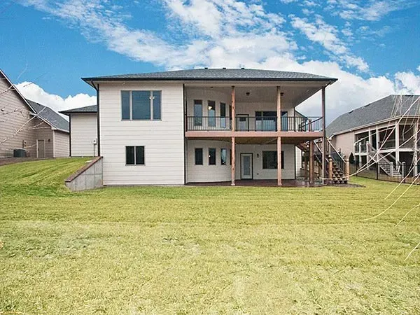 Two-story house with a large grassy backyard and covered rear porch under a blue sky.