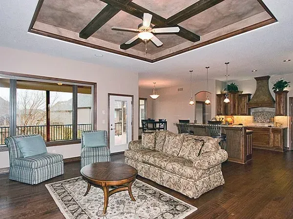 Spacious living room and kitchen with vaulted ceiling, floral sofa, blue chairs, dark wood floors, and patio view