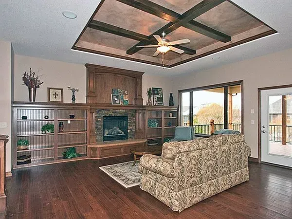 Spacious living room with wooden built-ins, patterned sofa, and ceiling fan under a tray ceiling.