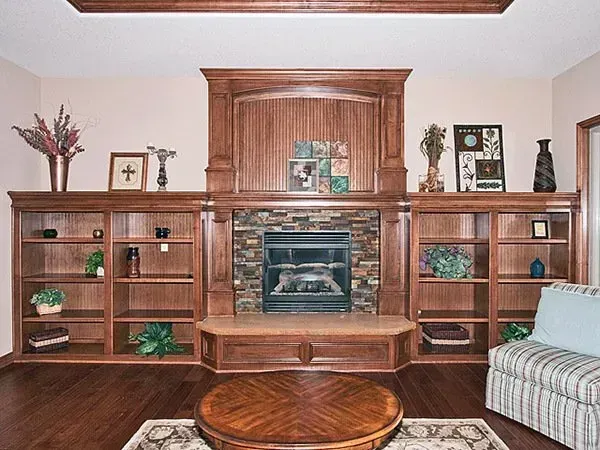 Living room wall unit with wooden shelves, a central fireplace, and a round coffee table