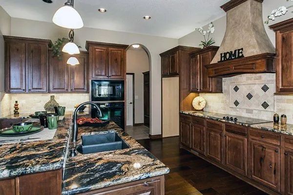 Modern kitchen with dark wood cabinets, granite island, pendant lights, and a decorative tiled backsplash