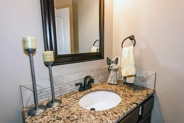 Bathroom vanity with granite countertop, round sink, mirror, and two candle holders