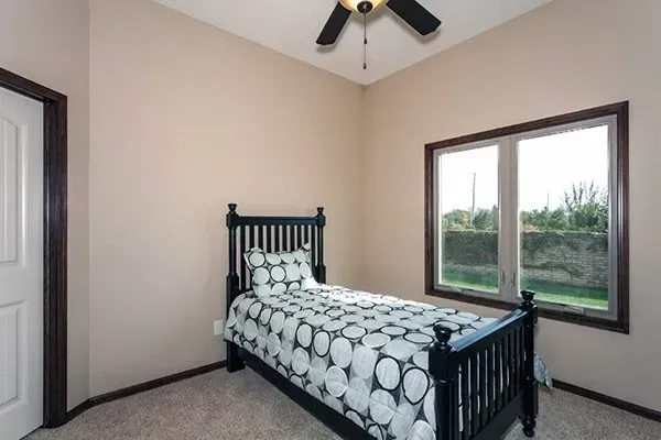 Small bedroom with a black bed, patterned bedding, beige walls, and a large window.