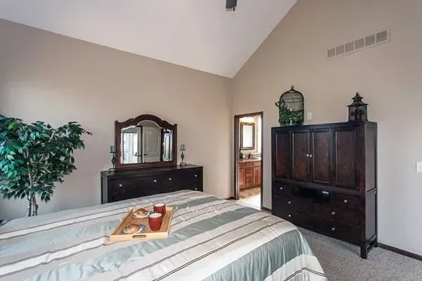 Bedroom with bed, dark wood dresser and armoire, mirror, and beige walls with vaulted ceiling.