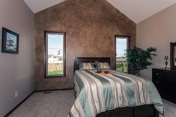 Spacious bedroom with a striped bedspread, two tall windows, and neutral-toned walls.