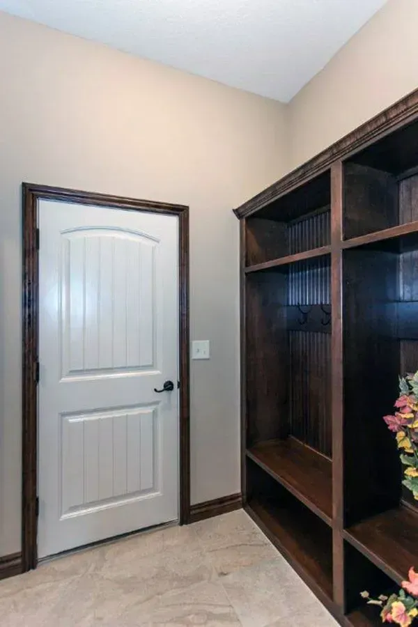 Closet or storage room with a white paneled door, beige walls, and a dark wood shelving unit.