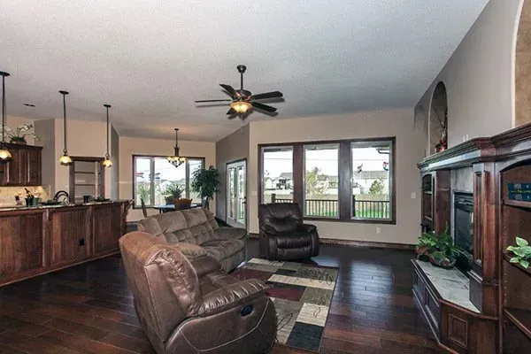 Spacious living room with leather sofas, dark wood furniture, ceiling fan, and large windows overlooking a deck