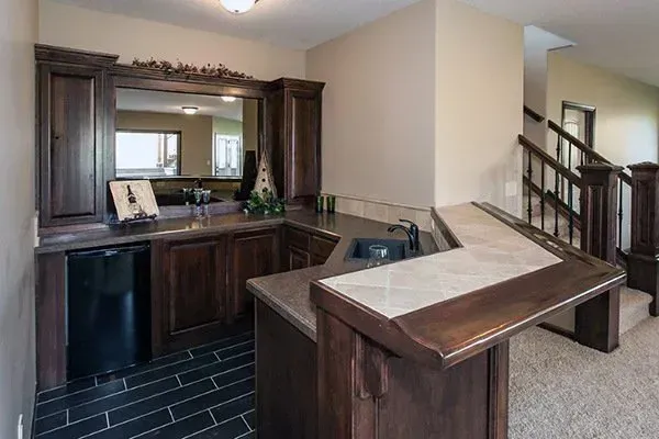 Living room with dark wood bar, black tile floor, and staircase in the background