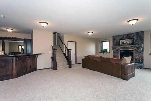 Spacious living room with brown sectional, fireplace, staircase, and wet bar in neutral tones