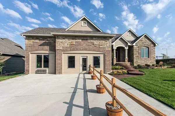 Modern brick house with a wide driveway, front porch, and wooden railing planters under a blue sky