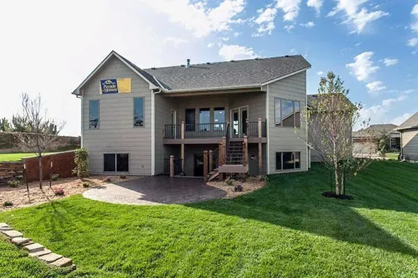 Backyard view of a two-story beige house with a large green lawn and patio deck