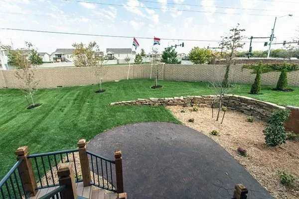 Backyard with green lawn, paved patio, curved garden bed, and a fence in the background