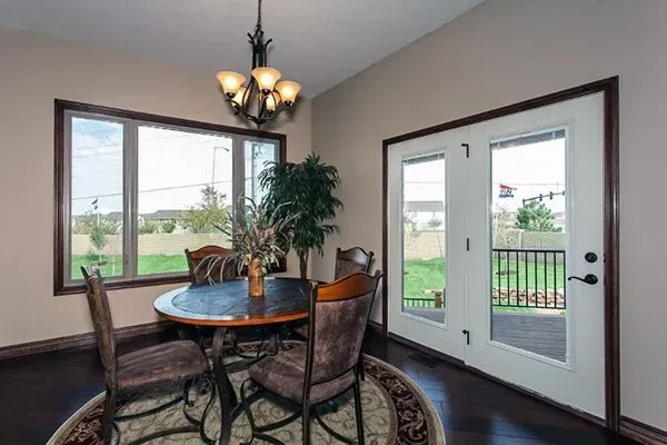 Dining nook with round table, four chairs, chandelier, windows, and French doors overlooking a green yard