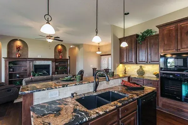 Spacious kitchen with dark wood cabinets, granite island, pendant lights, and adjacent living area.