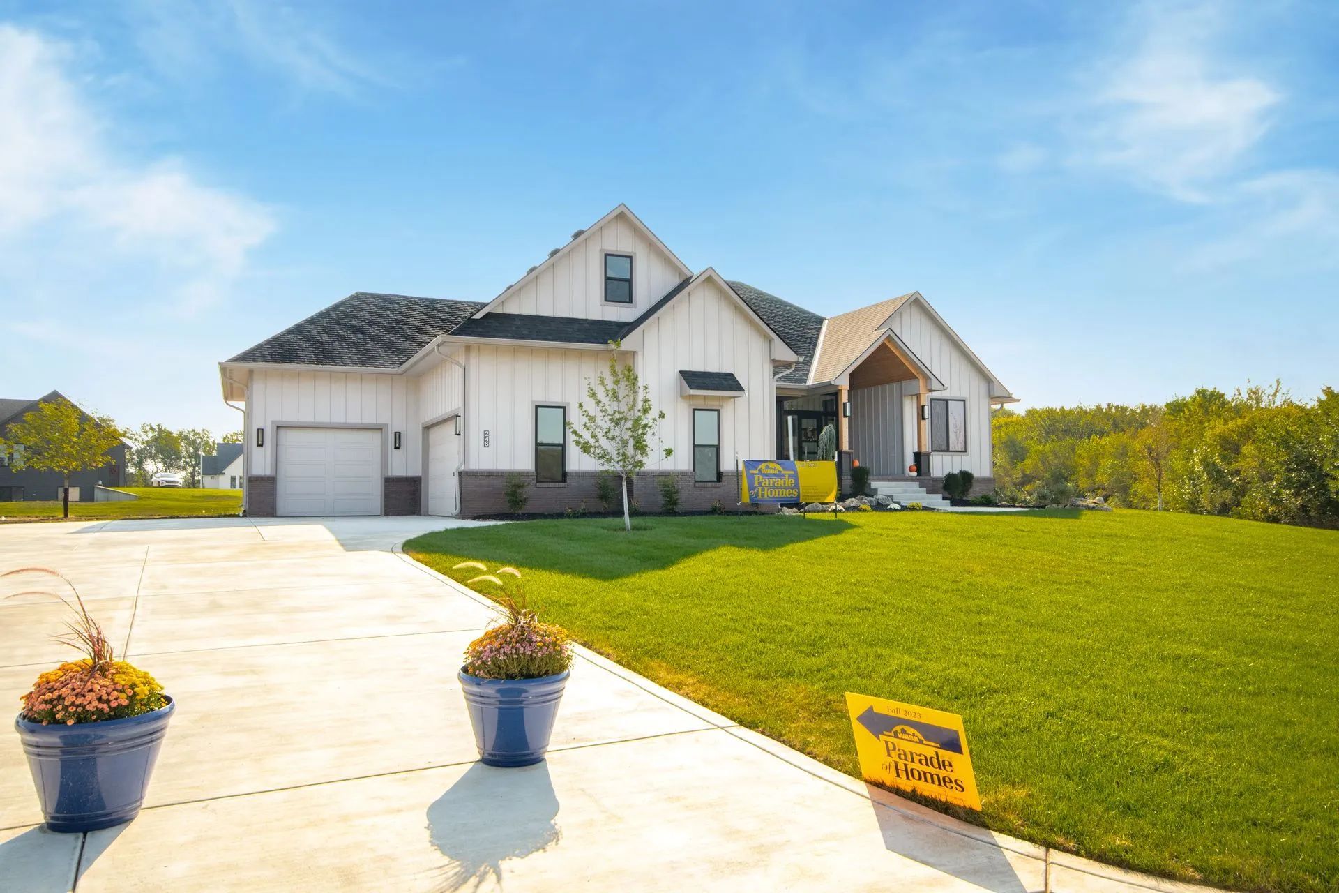 Suburban house with a three-car garage, landscaped lawn, and potted flowers on a sunny day