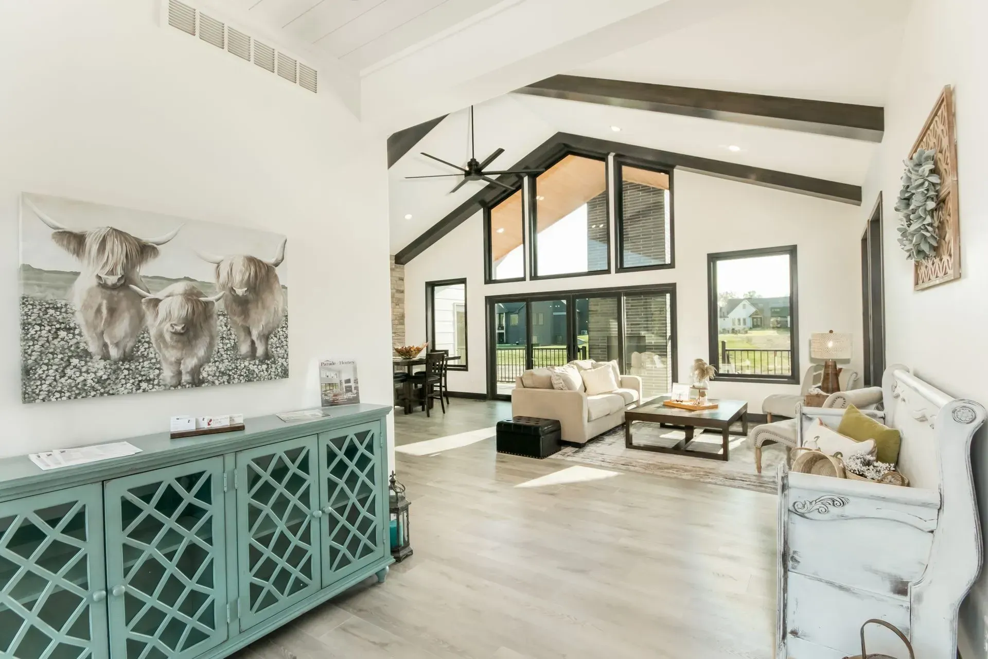 Bright modern living room with vaulted ceiling, large windows, white sofa, and teal console table
