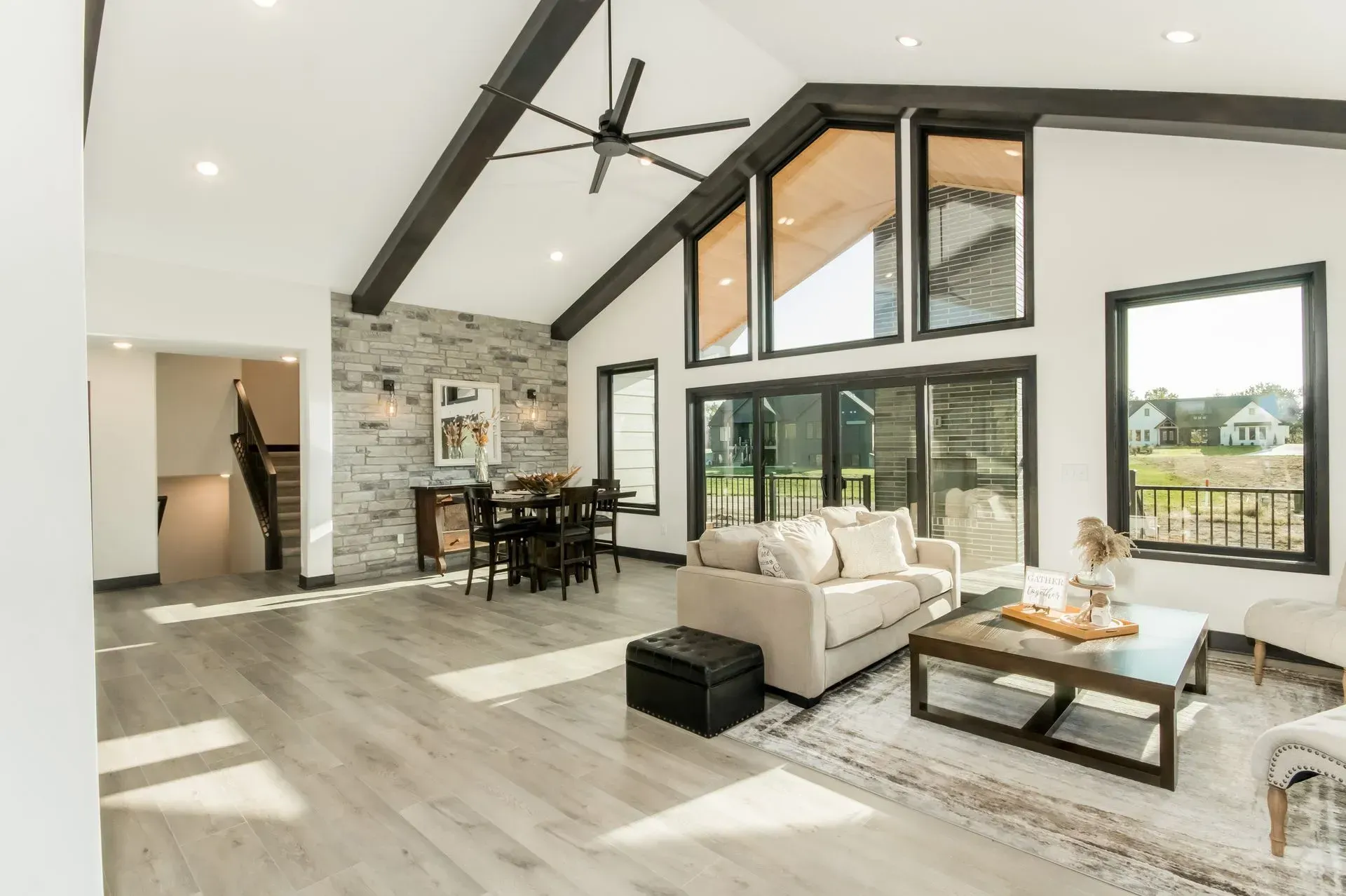 Bright modern living room with vaulted ceiling, stone fireplace, white sofas, and large windows