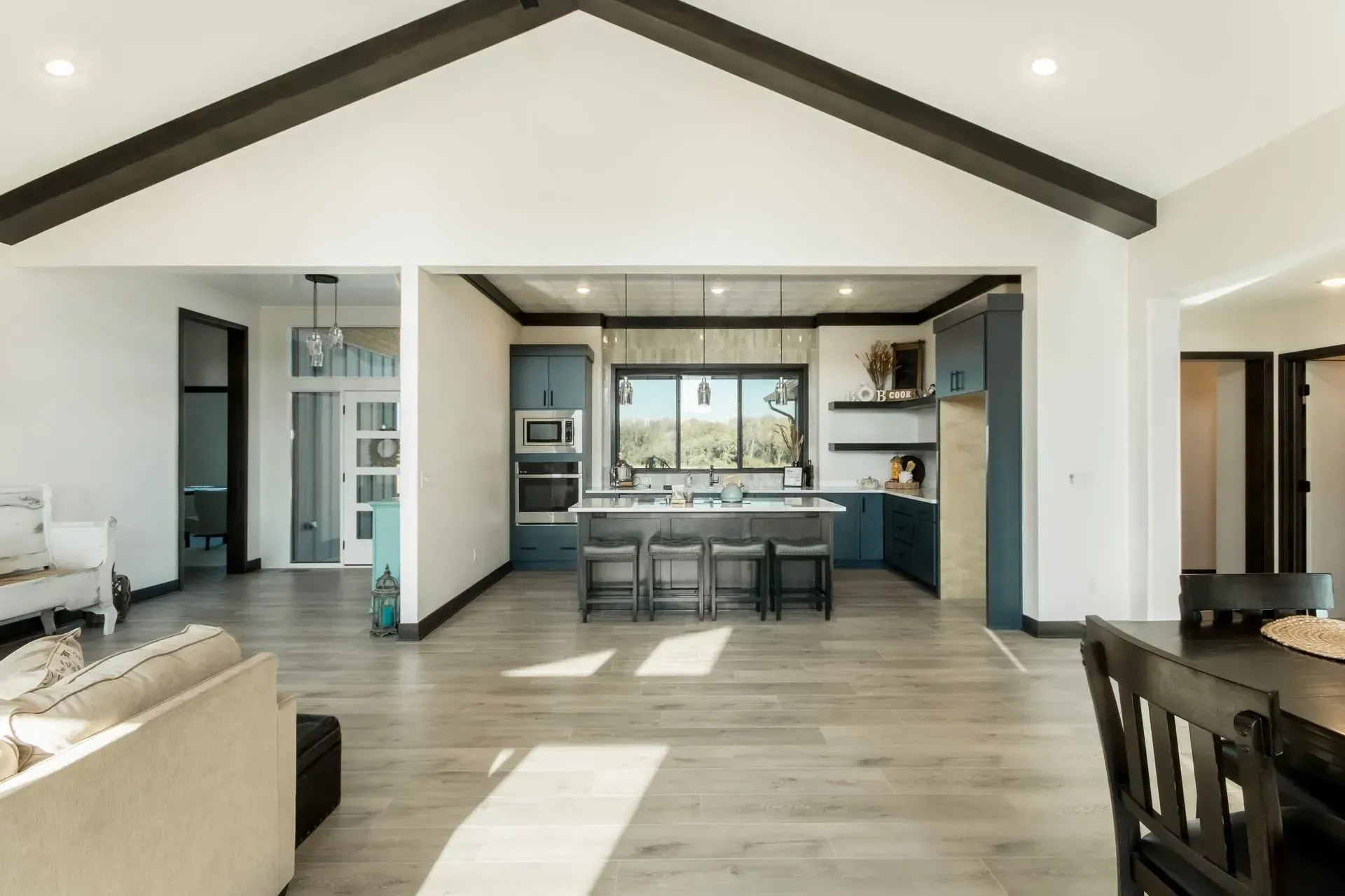 Open-concept living room and kitchen with vaulted ceiling, wood floors, and dark trim.