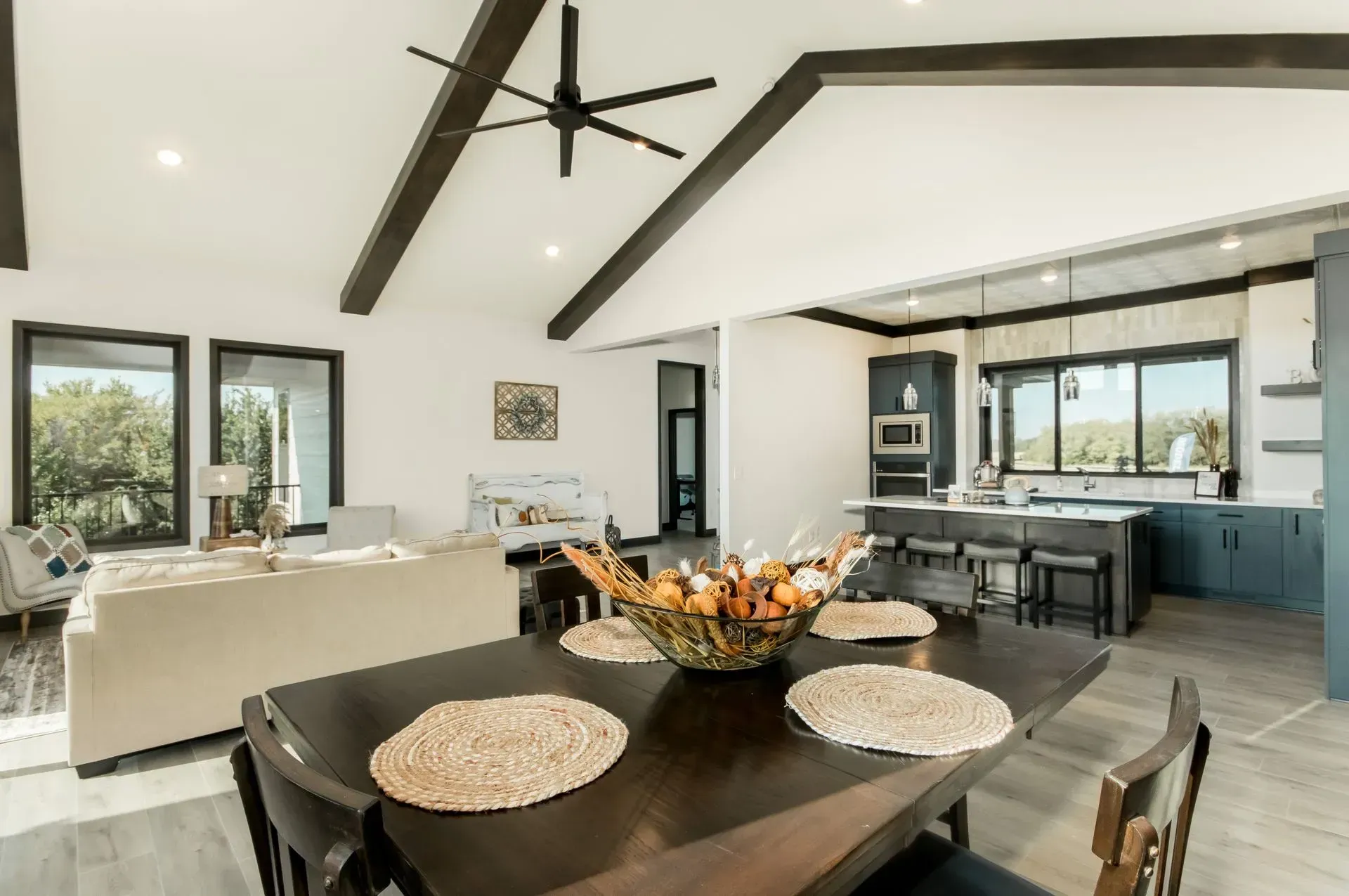 Open-plan modern kitchen and dining area with dark table, vaulted ceiling, and large windows