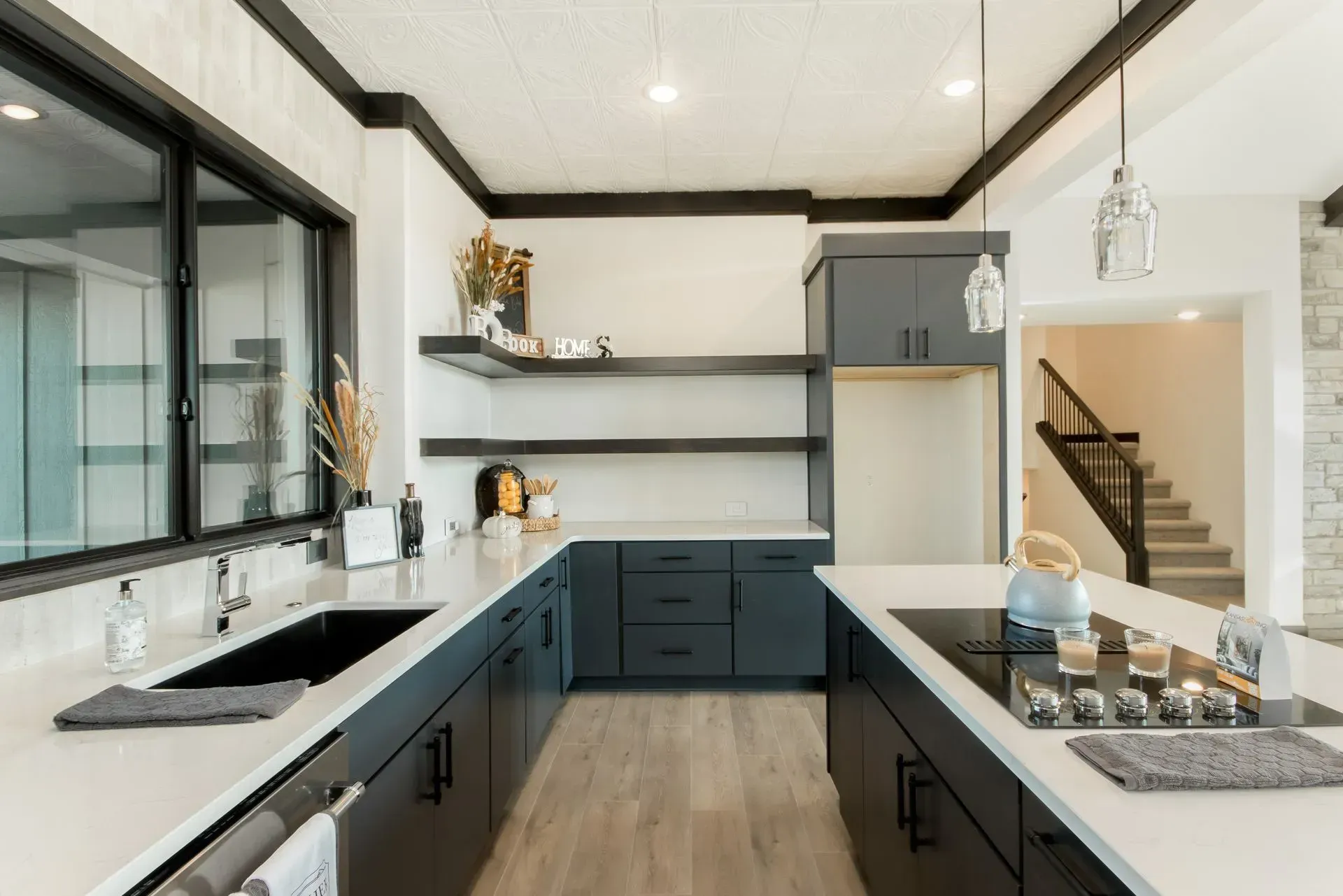 Modern bright kitchen with dark cabinets, white countertops, large window, and island with cooktop.