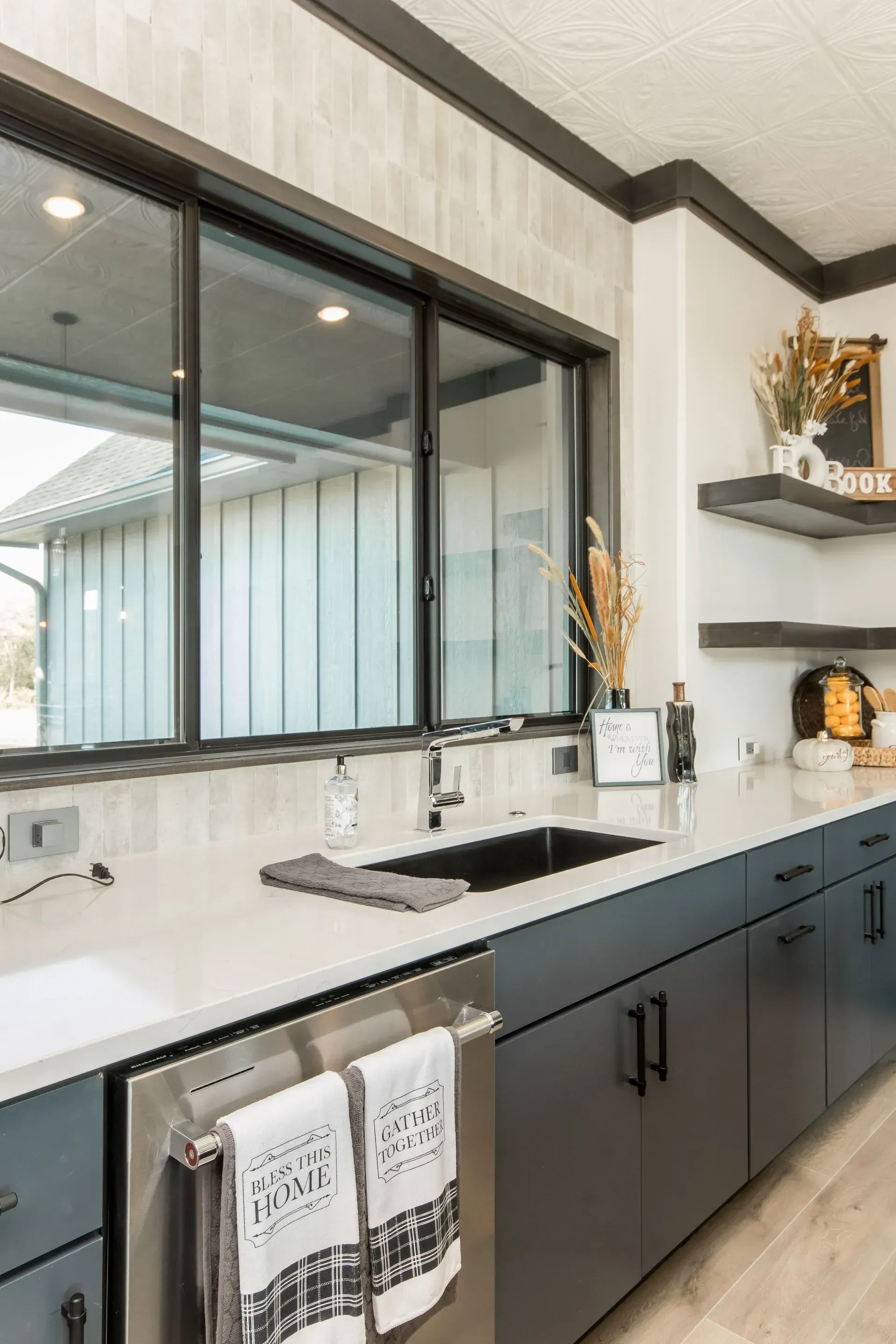 Modern kitchen with black cabinets, white countertops, and a large window above the sink.