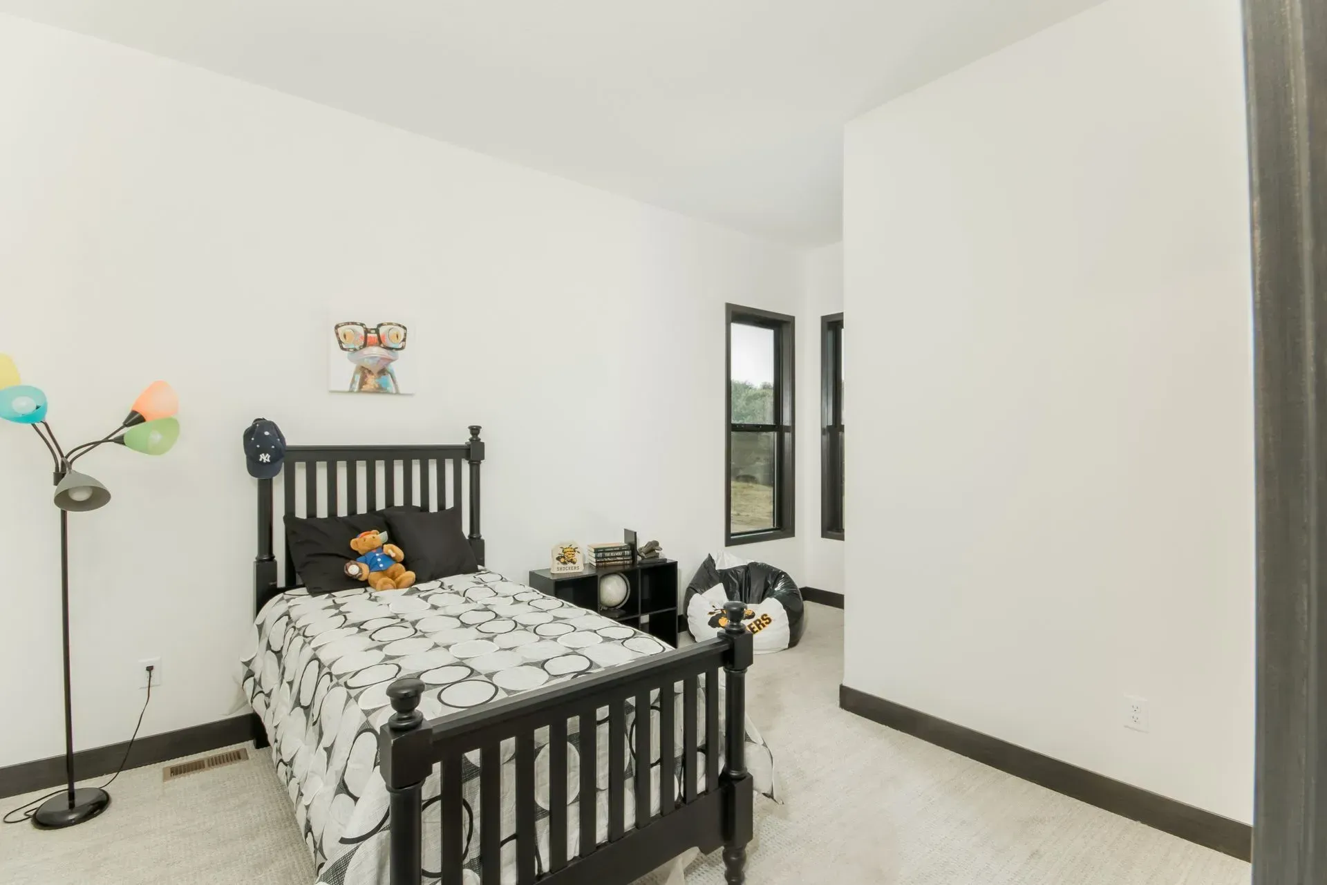 Small bedroom with black bed frame, patterned bedding, and a floor lamp near a window.