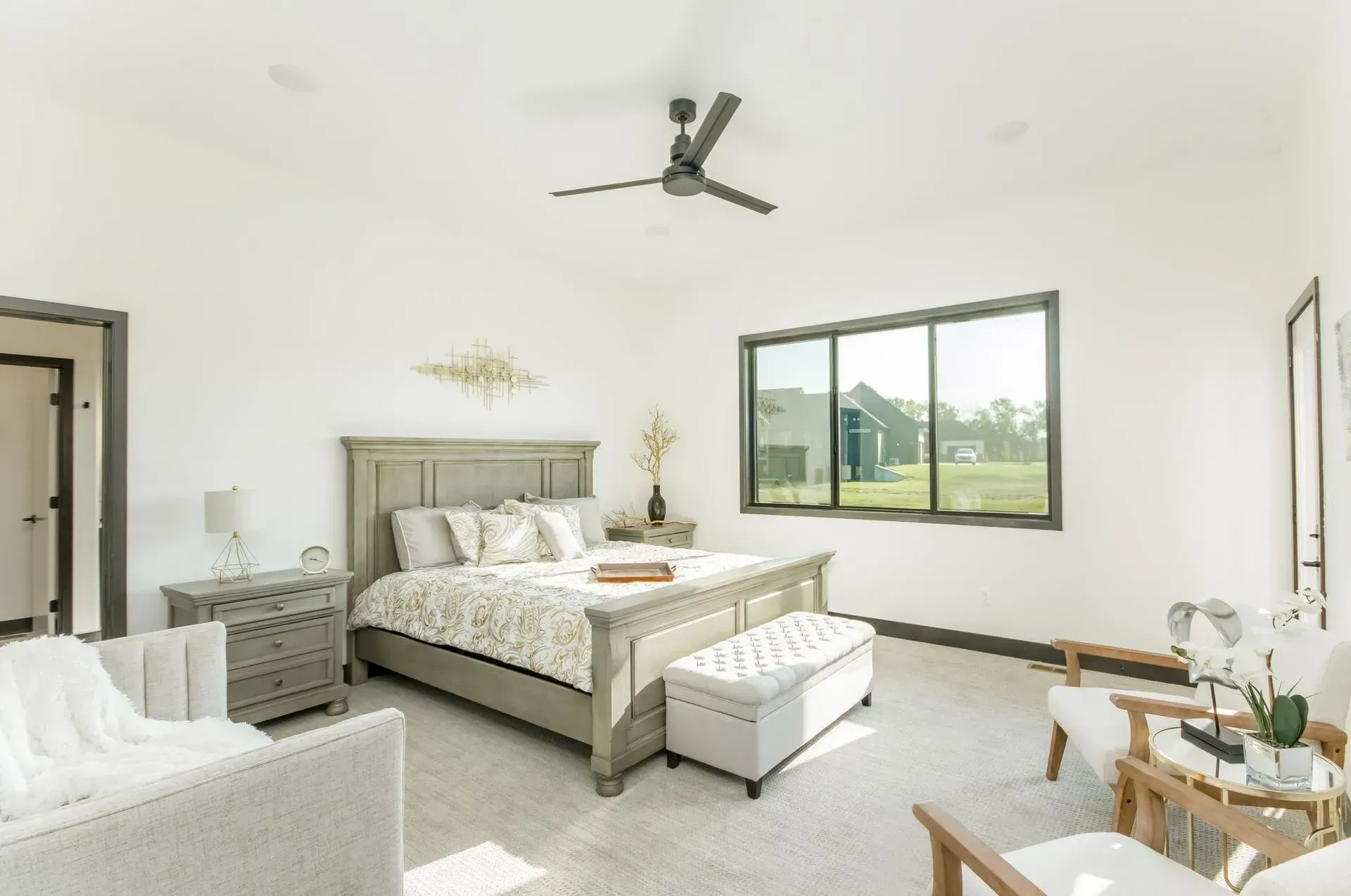 Bright modern bedroom with a bed, ceiling fan, and large window overlooking a suburban view