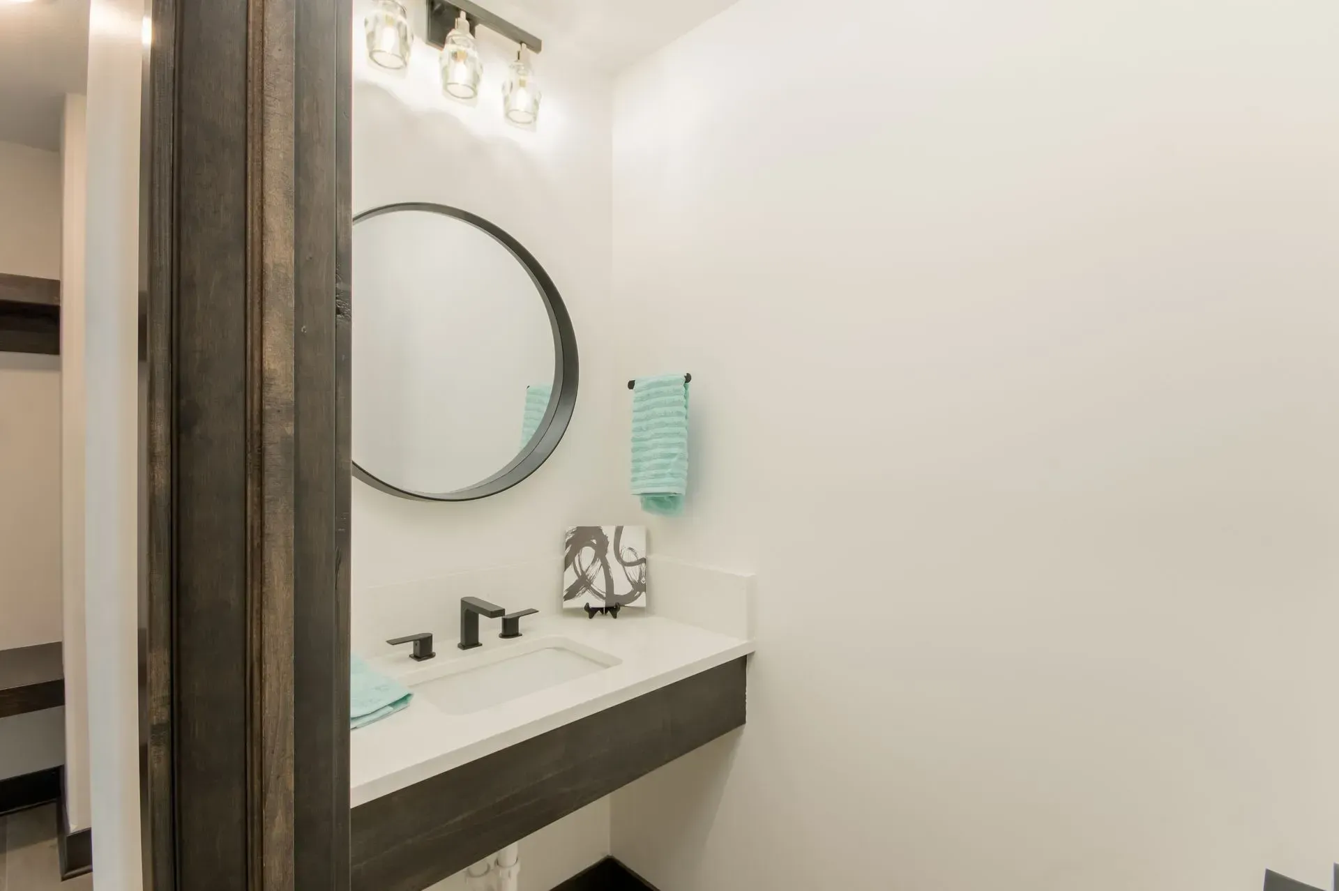 Small modern bathroom vanity with round mirror, wall light, and white sink counter