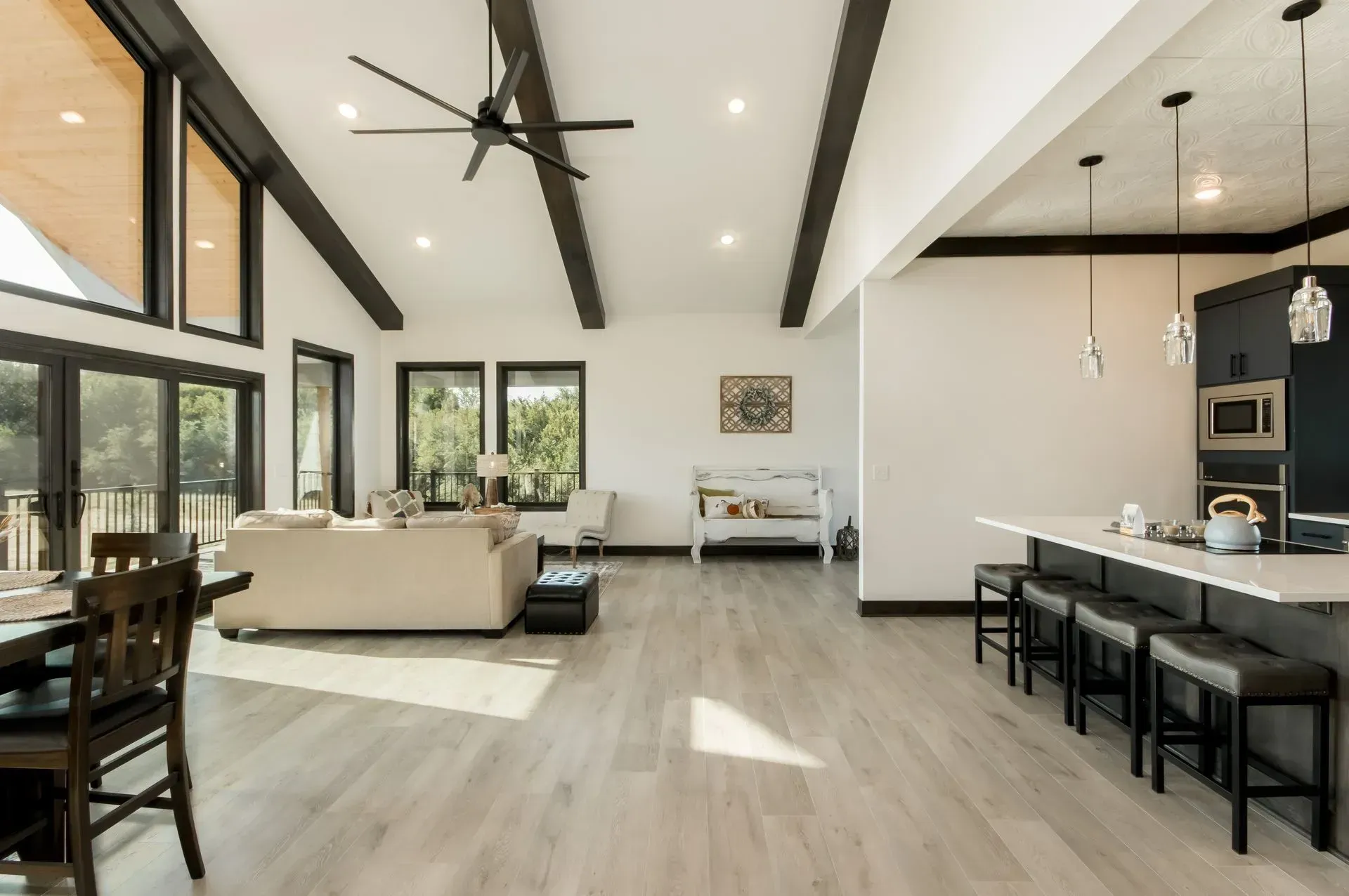 Open-concept modern living room and kitchen with high ceilings, black ceiling fan, and light wood floors