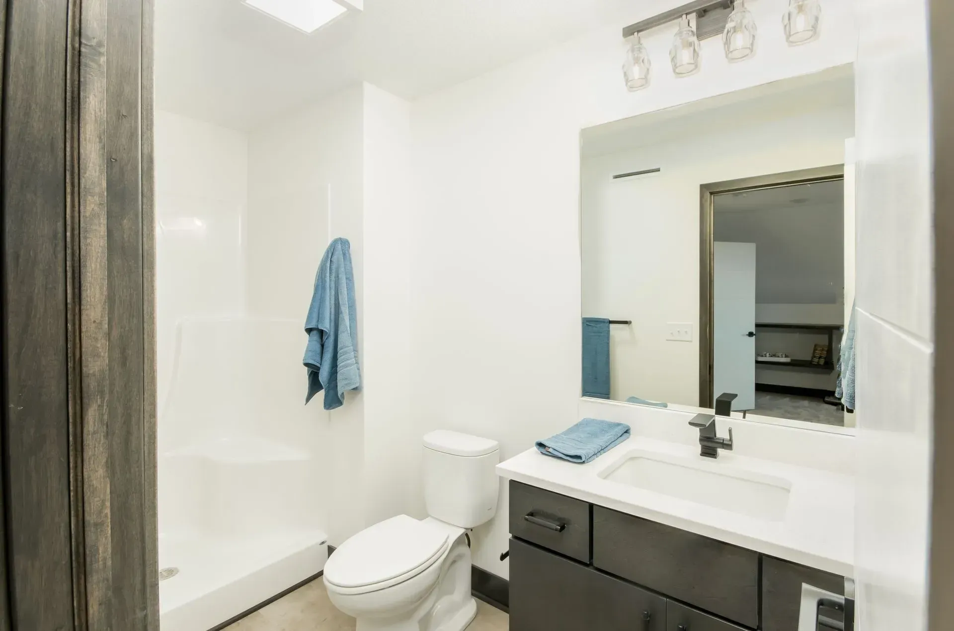 Bright bathroom with shower-tub combo, toilet, dark vanity, and large mirror